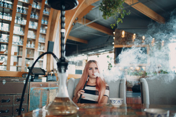 Fototapeta na wymiar Young beautiful female smoking hookah. Smoke shisha hookah in cafe concept.