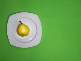 pear in white plate on green background