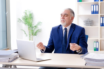 Aged businessman doing yoga exercises in the office 