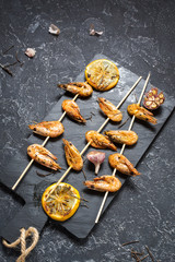 Grilled shrimp skewers with herbs, garlic and lemon on stone background. Seafood, shelfish.