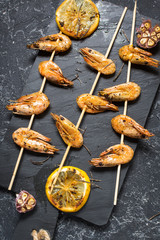 Grilled shrimp skewers with herbs, garlic and lemon on stone background. Seafood, shelfish.