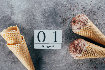 Chocolate ice cream in waffle cones and calendar date 01 August on gray background. Summer Dessert. Close-up, top view