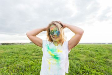 Fun, holi festival and holidays concept - Funny woman covered with color powder smiling over nature background