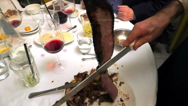 Close up of loin cutting with a knife on the spit. Blurred table in Brazilian restaurant background.
