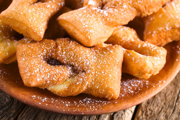 Traditional Chilean sweet calzones rotos deep-fried pastries sprinkled with powdered sugar served on wooden plate (Selective Focus, Focus on the front of the first pastry)