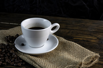Cup of coffee and coffee beans on a rough wooden background.