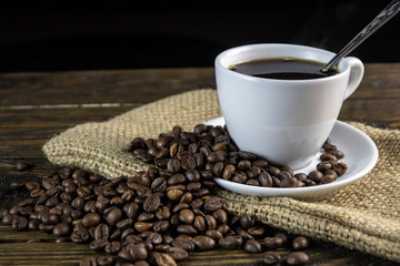 Cup of coffee and coffee beans on a rough wooden background.