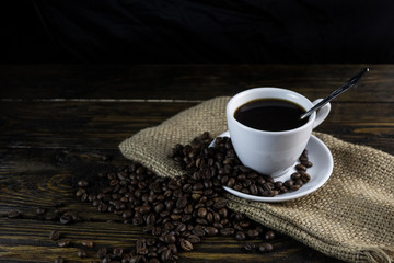 Cup of coffee and coffee beans on a rough wooden background.