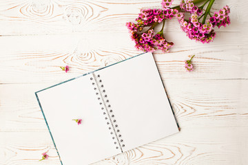 Naklejka premium Blank diary for your text and pink flower on a white wooden table. Flat design