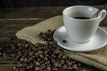 Cup of coffee and coffee beans on a rough wooden background.