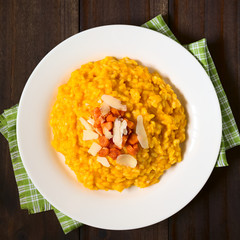Fresh homemade carrot risotto made with pureed carrot, garnished with roasted carrot and hard cheese, photographed overhead on dark wood with natural light (Selective Focus, Focus on the risotto)