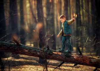 Beautiful little boy in a green sweater, denim jacket and rubber boots walks in the woods on a dry...