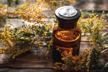 Mimosa flower essential oil bottle on a wooden board background. Herbal medicine.