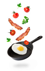 Fried egg, bacon and cherry tomatoes flying into iron skillet