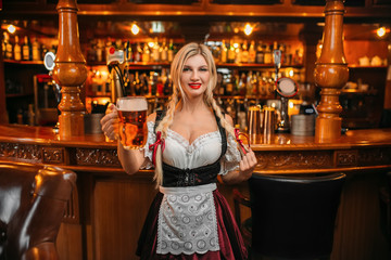 Sexy waitress holds two mugs of fresh beer in pub