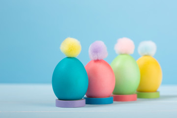 Dyed bright Easter eggs in stands with colorful pompons on a blue background.