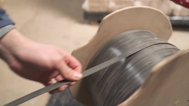 A close-up of a worker taking plastic wrapping rope from a spool to pack the briquettes