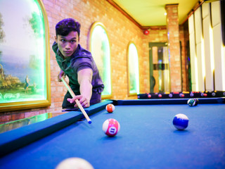 Fototapeta premium Young man play billiards in the colorful club - Aiming white ball to shot