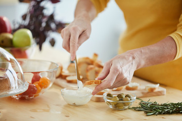 Close-up of unrecognizable woman buttering bread with knife while making appetizers in kitchen