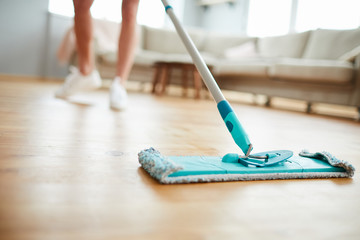 Close-up of unrecognizable woman using mop with microfiber pad while cleaning parquet floor in...