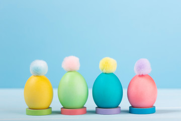Dyed bright Easter eggs in stands with colorful pompons on a blue background.