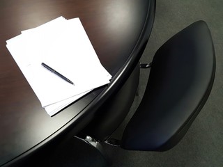 A bundle of paper documents is under the pen on the desk of the black office in anticipation of the signature.