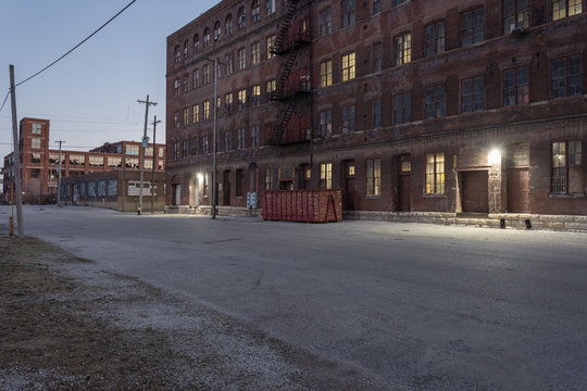 Down An Industrial Street Behind A Vintage Multiple Story Red Brick Warehouse With Lights