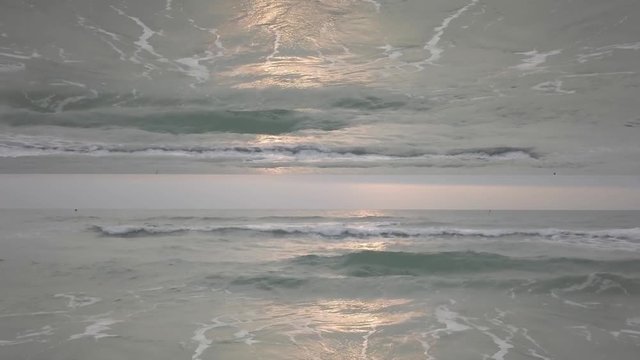 Beautiful seascape with horizon mirror effect with waves crashing on the shore. Endless waves with sun reflection on water surface, inception theme.