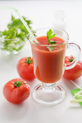Tomato juice is poured into a transparent glass with parsley and herring, on a white background with cherry tomatoes, lit by sunlight