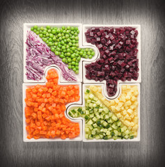 .Raw vegetables carrots, peas, onions, cucumber, potatoes, beets cut into cubes lie on puzzles in the form of puzzles and gather in a single large dish.