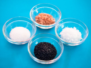 Crystal bowls with himalayan salt, black hawaii salt, common salt and salt flakes on a blue background