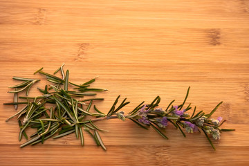One rosemary blooming twig and rosemary leaves on a wooden table