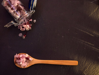 A glass jar full of edible flowers and a wooden spoon with edible flowers on a slate plate