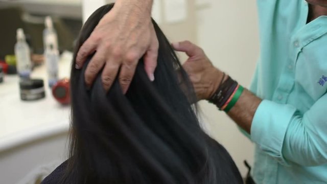 Hairdresser plays with beautiful long black hair in his fingers in beauty saloon