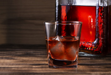 glass of whiskey with bottle on wooden background