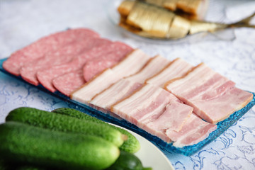 On white table is snack for vodka, in the form of fresh cucumbers, chopped smoked sausage and a bowl of fish lying with a ryadoch.