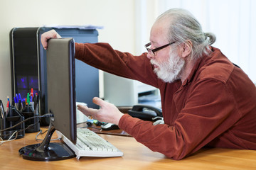 Serious senior man trying to use computer, holding monitor with understanding. Aged people with new...
