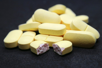Fototapeta na wymiar Pills pile one broken large yellow macro photo on black background.