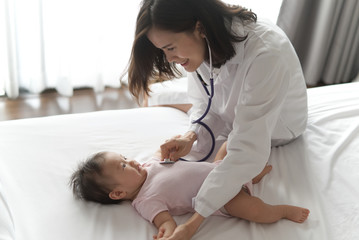 Obraz premium Female doctor is listening heart pulse rate of cute newborn baby on the bed by using stethoscope in the room. Seen from top view. Baby health care concept.