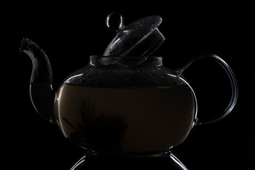 glass teapot with boiling water and an open lid on the walls, a drop of steam inside the teapot green tea. photo in a dark key on a black background. in the photo the contours of the kettle