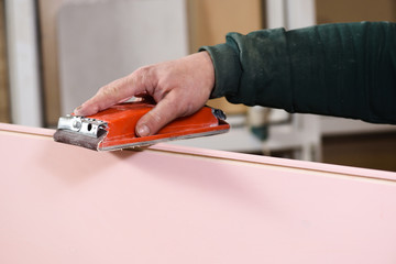 Carpenter hands sanding pink plywood detail with sandpaper holder