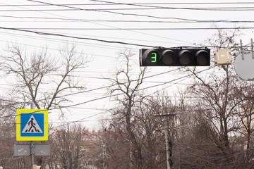 traffic light glowing green. The next color is 3 seconds away. Also in the background there is a sign of a pedestrian crossing.