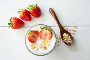 Top view of Greek yogurt with fresh strawberries and muesli on white wooden background. Decorated with some pieces of strawberries and wooden spoon of muesli. Fresh food for breakfast concept.