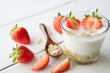 Greek yoghurt with fresh strawberries and muesli on white wooden background. Decorated with some pieces of strawberries and wooden spoon of muesli. Fresh food for breakfast concept.