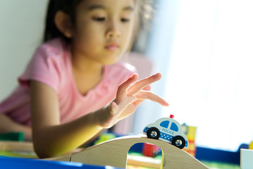 Young little Asian cute kid playing wooden toy on table at home. She is  pushing a car running on the wooden rail. Creativity and development toy for kid. Play and learn concept.