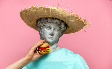 Antique bust of male in hat with hamburger on pink background