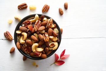 Mix nuts and dried fruits background and wallpaper. Seen in top view of mix nuts and dried fruits in the bowl decorated with some nuts and red leaf on white wood in background.