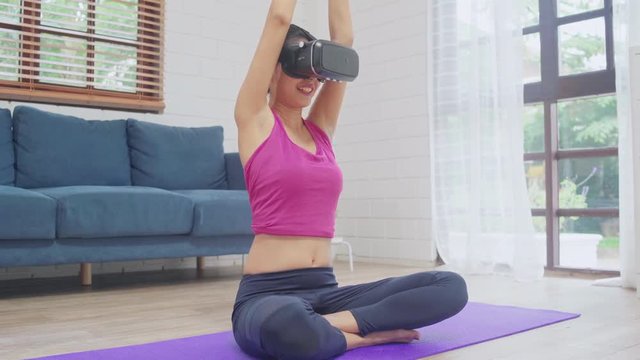 Young Asian teenager woman using virtual reality simulator while practicing yoga in living room, female working out for healthy at home. Lifestyle woman exercise future technology concept concept.
