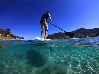 Underwater sea level photo of unidentified man on a SUP or Stand Up Paddle in turquoise crystal...
