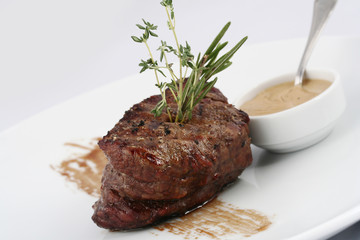  Delicious steak medium rare with rosemary leaves and sauce on a white background.